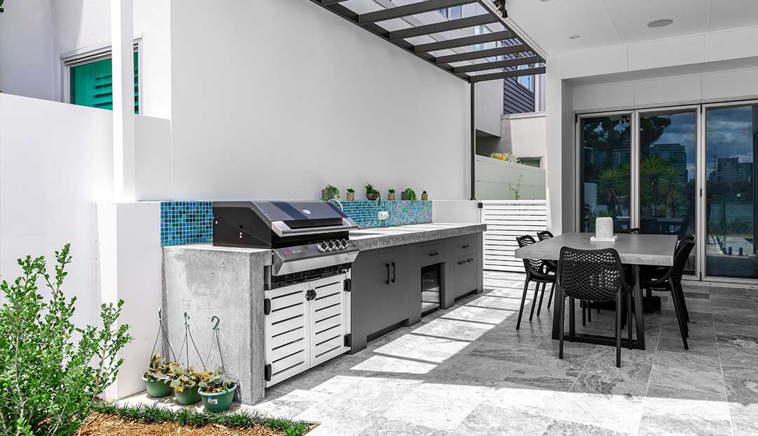 Stone outdoor kitchen with a BBQ grill and mosaic tile backsplash.