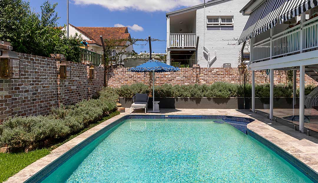 A serene backyard pool area on Emlyn Street, Brisbane, featuring a lush garden and brick wall for privacy and relaxation.