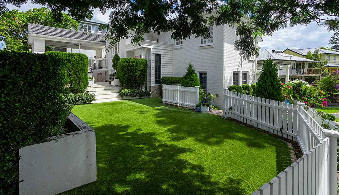 Brisbane Citys lush green lawn of a white suburban home with hedges.